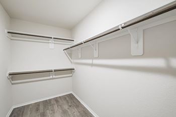 A spacious walk in closet with white walls and wood flooring