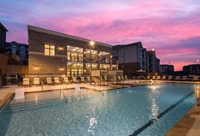 Huntersville apartment for rent - A large swimming pool in front of a building with a sunset in the background.