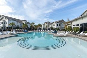 Savannah apartment for rent - Two-Bedroom Apartments in Downtown Savannah, GA - Adara at Godley Station - Large Swimming Pool Surrounded by Sun Loungers, Cabanas, Umbrellas, Outdoor Couch, Landscaping, and a View of the Apartments.