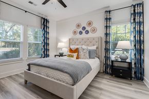 Charleston apartment for rent - Dog-Friendly Apartments in Charleston, SC - The Avenues at Verdier Pointe - Bedroom with Wood-Style Flooring, Ceiling Fan, Bed, Nightstands, Lamps, and Large Windows with Blinds and Curtains.