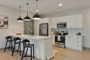 Grandville apartment for rent - A kitchen with white cabinets and a white island with black barstools.
