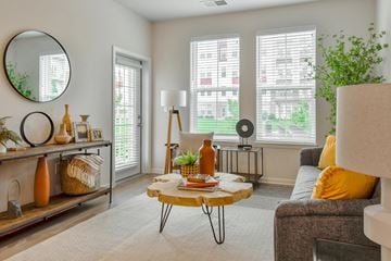 Lansing apartment for rent - A living room with a grey couch, a round mirror, and a table with a plant on it.