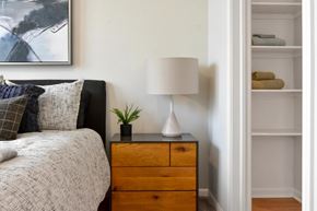 Lansing apartment for rent - A bedroom with a bed, a nightstand with a lamp, and a shelf with towels.