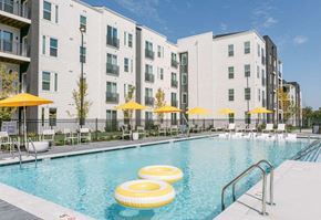 Madison apartment for rent - A swimming pool with yellow umbrellas and floating yellow chairs in front of a white building.