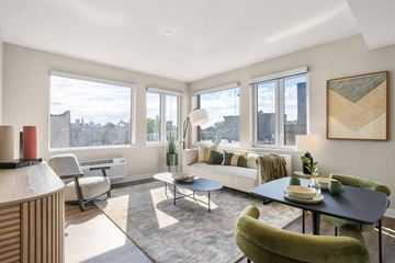 West New York apartment for rent - A living room with a green chair and a table with a vase of flowers on it.