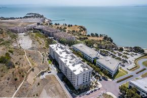 San Francisco apartment for rent - A large white building is surrounded by a parking lot and a hill with a fence.
