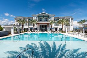 Orlando apartment for rent - The pool area at Corban Freedom Apartments in Orlando, FL, featuring lounge chairs, a shade structure, and palm trees.