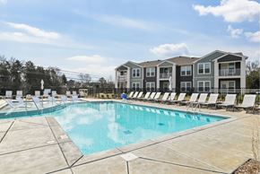 Charlotte apartment for rent - A large swimming pool in front of a building with lounge chairs around it.