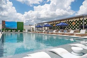 Austin apartment for rent - A pool with white chairs and umbrellas is surrounded by a building with a green wall.
