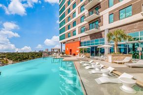 Houston apartment for rent - A large swimming pool with white chairs is in front of a modern building.