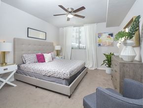 Miami apartment for rent - A bedroom with a large bed, a ceiling fan, and a chair.