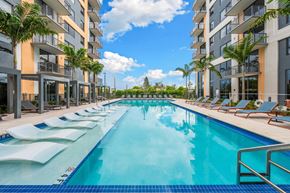 Miami apartment for rent - A long rectangular swimming pool with lounge chairs on the side.