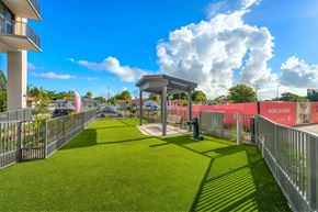 Miami apartment for rent - A grassy area with a small shelter and a fence with "NOW LEASING" written on it.