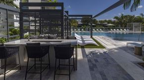 Miami apartment for rent - A modern outdoor dining area with a table and chairs overlooking a pool.