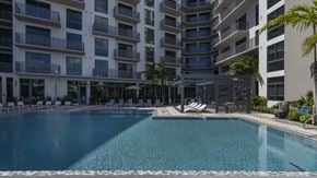 Miami apartment for rent - A large swimming pool in front of a multi-story residential building.