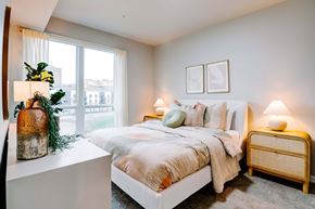 Kansas City apartment for rent - A bedroom with a large bed, a nightstand, and a window with a view of the city.