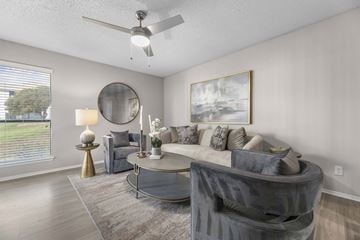 Fort Worth apartment for rent - A living room with a grey couch, a round mirror, and a painting on the wall.
