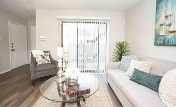 Houston apartment for rent - A living room with a grey armchair, a glass coffee table, a white sofa, and a painting on the wall.