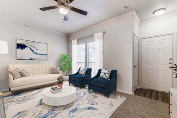 Mesquite apartment for rent - A living room with a white couch, blue chair, and a painting on the wall.