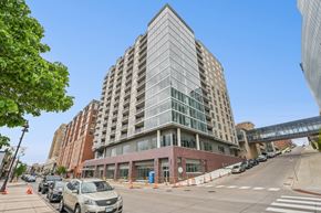 Duluth apartment for rent - A modern glass building is situated on a street corner with cars parked on the side.