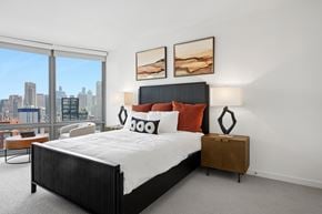 Chicago apartment for rent - A bedroom with a large bed and a city view through the window.