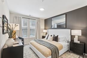 Hyattsville apartment for rent - A bedroom with a large bed, a nightstand with a lamp, and a mirror above the bed.