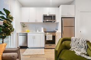 Philadelphia apartment for rent - a living room with a green couch and a kitchen with white cabinets and stainless steel appliances