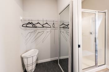 A closet with a mirror and a trash can in a bathroom with a glass shower