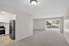 Tampa apartment for rent - A spacious living room with a carpeted floor and a view of the outdoors through a sliding glass door. at Foxcroft Apartments, Tampa, 33614