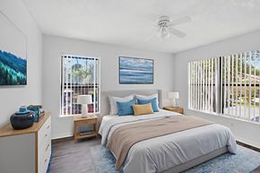 Naples condo for rent - A bedroom with a large bed, a ceiling fan, and a painting of a beach scene on the wall.