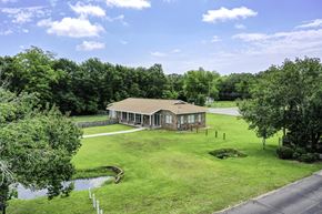 Pensacola condo for rent - A house with a brown roof is surrounded by a green lawn and trees.