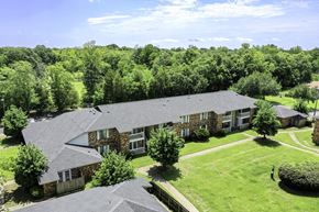 Pensacola condo for rent - A large house with a grey roof surrounded by a green lawn and trees.