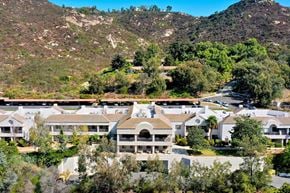 Poway apartment for rent - A large white building with a balcony is surrounded by trees and hills.