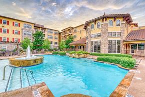Dallas apartment for rent - A large outdoor swimming pool with a fountain in the middle of it.