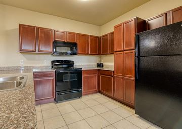 Dallas apartment for rent - A kitchen with brown cabinets and black appliances.