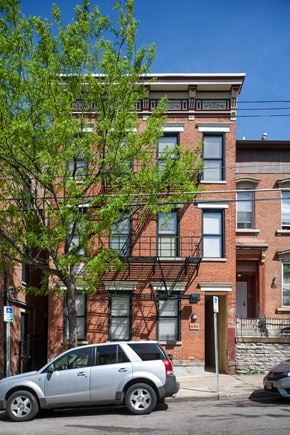 Cincinnati apartment for rent - A silver car is parked on the street in front of a red brick building.