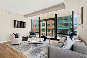 Minneapolis apartment for rent - A living room with a grey couch, a white coffee table, and a large window with a view of a building.