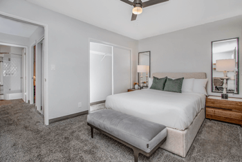 A spacious bedroom with a large bed, sitting bench, plush carpet, and a ceiling fan