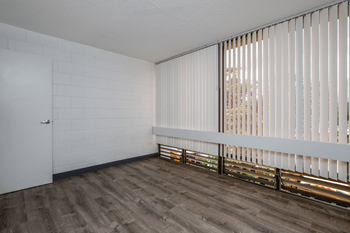 An empty living room with white vertical blinds on the oversized windows