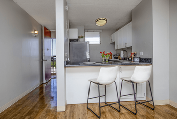 A kitchen with white cabinets and a counter with two chairs at the breakfast bar