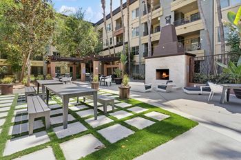 A patio with a table and chairs is surrounded by a grassy area and apartment buildings.