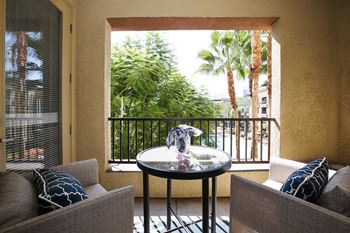 A balcony with a table and two chairs overlooking a lush green area.