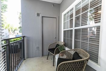 A balcony with two wicker chairs and a door to a patio