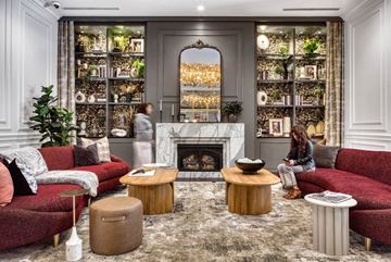 Chicago apartment for rent - A woman is sitting on a red couch in a living room with a fireplace and shelves filled with plants.