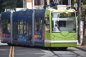 A green and blue tram is on the tracks
