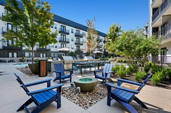 A sunny day at a courtyard with blue chairs and a fire pit.