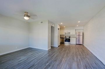 Phoenix apartment for rent - A kitchen with white cabinets and a refrigerator is visible through an open door in a room with wooden floors.