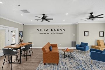 Yuma apartment for rent - A living room with a sofa, chairs, and a dining table with a sign that says "VILLA NUEVA APARTMENTS".