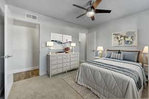 Mesa apartment for rent - A bedroom with a large bed, a dresser, and a ceiling fan at Gilbert Square Apartments, Mesa, AZ