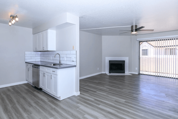 Spacious living room with plank flooring, sliding glass doors that lead to the patio, view into kitchen, and fireplace 